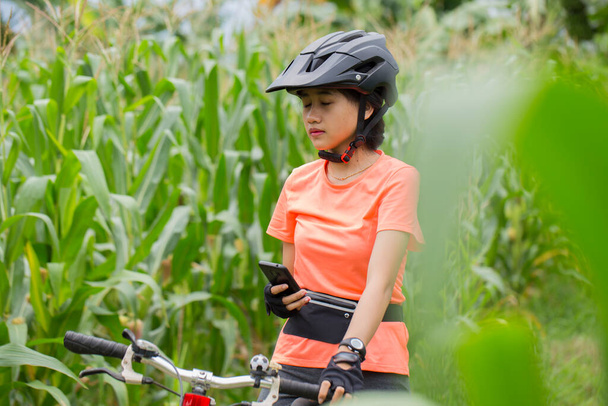 Ázsiai nő kerékpáros használni okostelefon, amikor lovaglás kerékpár a városi erdőben. - Fotó, kép