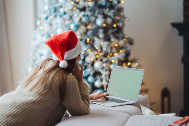Female wearing santa hat while speaking with online friend on laptop - Foto, immagini