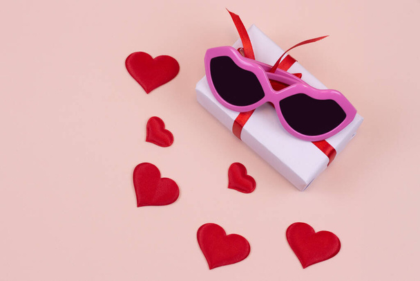 roze zonnebril en hartjes met een cadeau op een lichte achtergrond. Kopieerruimte - Foto, afbeelding