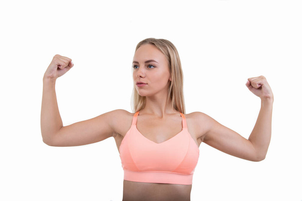 A young woman in a pink top shows her muscles on a white background - Фото, изображение