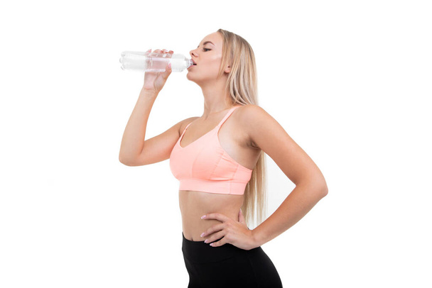 Een jonge vrouw in een roze top drinkt water na een training - Foto, afbeelding