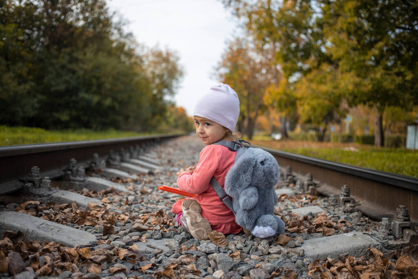 schattig peuter meisje zit op de spoorweg alleen op een zomerdag, gevaarlijke situatie - Foto, afbeelding