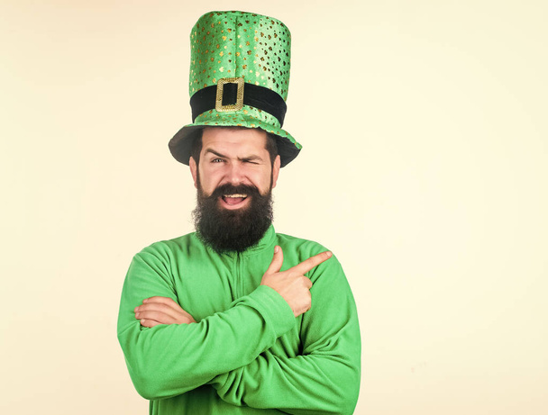 Pointing his finger at something. Hipster in leprechaun hat and costume. Irish man with beard wearing green. Bearded man celebrating saint patricks day. Happy saint patricks day, copy space - Фото, изображение