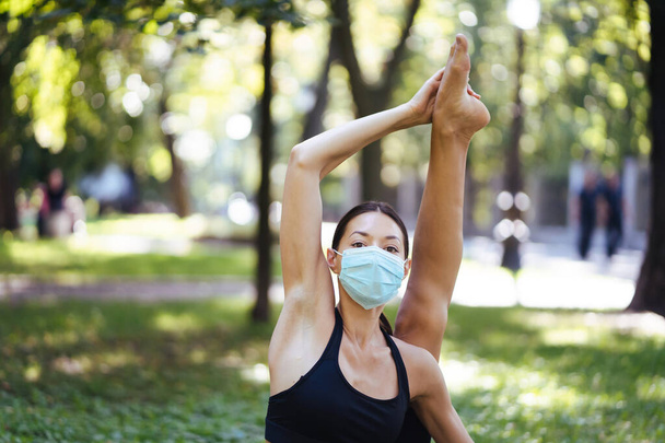 Sportos fiatal nő orvosi védőmaszkban, jógázik a parkban - Fotó, kép