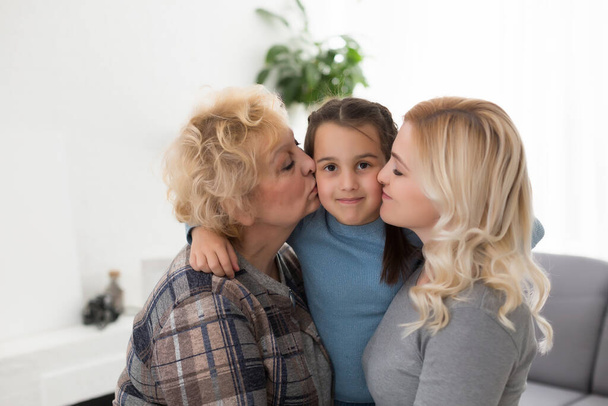 Tre generazioni di donne. Bella donna e adolescente ragazza stanno baciando la nonna mentre si siede sul divano a casa - Foto, immagini