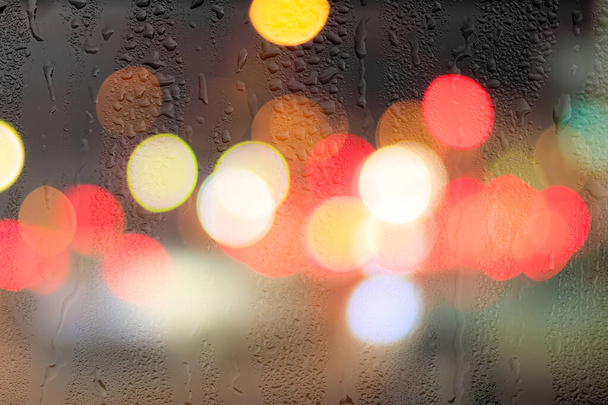 Luces nocturnas de la ciudad y faros de coche a través de vidrio lluvioso. Lluvia y mal tiempo húmedo concepto. - Foto, Imagen