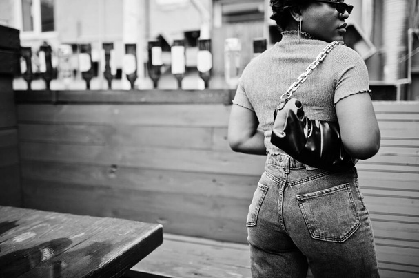 Urban young african american woman in pink top and grey jeans with handbag. Afro fashion chic women back buttocks. - Foto, immagini