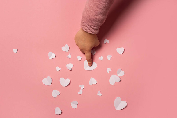 Child's hand takes a valentine card from paper on a pink background. Composition Valentine's Day. Banner. Flat lay, top view. - Photo, image