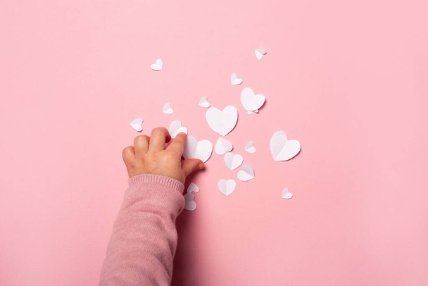 Kind neemt een valentijnskaart van papier op een roze achtergrond. Samenstelling Valentijnsdag. Een spandoek. Vlakke lay, bovenaanzicht. - Foto, afbeelding