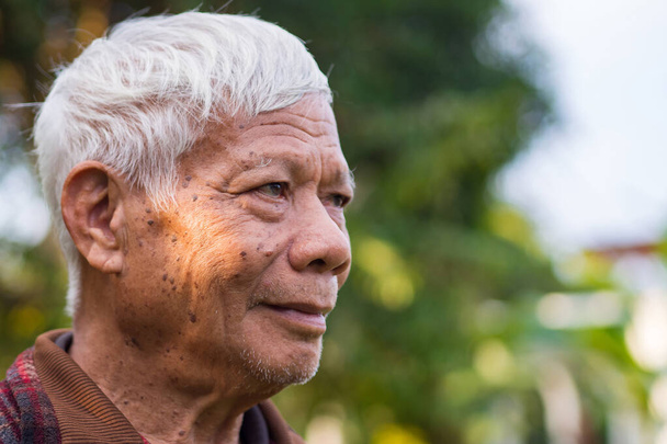Portret starszego Azjaty uśmiechającego się i spoglądającego w górę, stojącego w ogrodzie. Miejsce na tekst. Pojęcie osób w podeszłym wieku i opieki zdrowotnej. - Zdjęcie, obraz