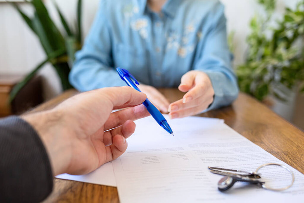 An employee gives the client a pen to fill out documents. Hands close-up. There are papers and keys on the table. Rental and purchase of real estate. - Foto, Imagem