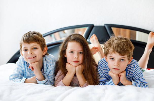 Tre bambini felici in pigiama che festeggiano il pigiama party. prescolare e scuola ragazzi e ragazza divertirsi insieme - Foto, immagini