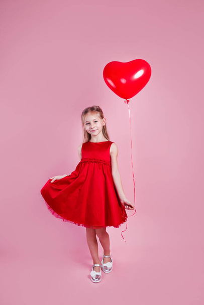Valentines day. Little girl in red dress with heart shape air balloon on pink background - Foto, Imagem