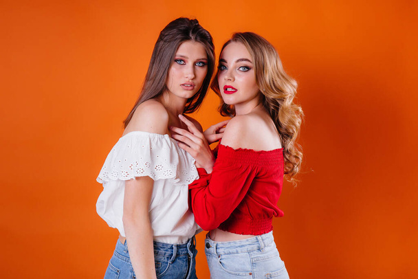 Two young and beautiful girls shows emotions and smiles in the Studio on an orange background. Girls for advertising - Фото, изображение