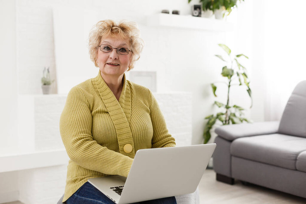 ευτυχισμένη ηλικιωμένη γυναίκα που χρησιμοποιεί φορητό υπολογιστή στο σπίτι - Φωτογραφία, εικόνα