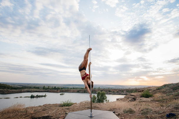 A young sexy girl performs amazing exercises on a pole during a beautiful sunset. Dance. Sexuality - Foto, Bild