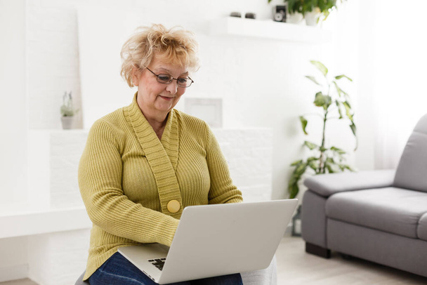Atrakcyjne starsza kobieta siedzi na kanapie w domu, patrząc w kamerę, sprawia, że połączenie wideo, komunikacja na odległość, nowoczesne technologie bezprzewodowe koncepcja - Zdjęcie, obraz