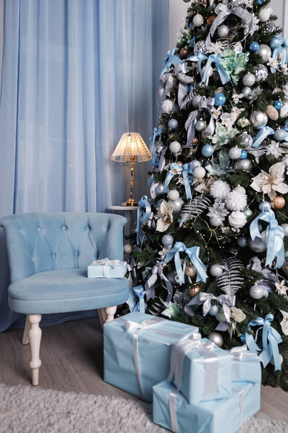 Beautifully packaged blue presents under the Christmas tree and blue armchair - Fotografie, Obrázek