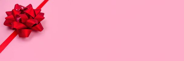 Banner con fiocco decorativo a nastro rosso su sfondo rosa con spazio per la copia del testo. Dare il concetto di regali. Biglietto di auguri o vacanze sfondo vendita, messa a fuoco selettiva - Foto, immagini