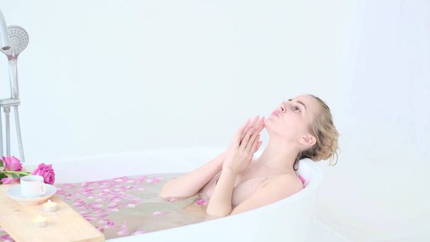 リゾート・デイ・スパ・サロンで花風呂に寝そべっているビキニの美しい白人ブロンドの女の子。スキンケア療法。コンセプト若いです女性リラックスでザバスチューブ. - 写真・画像