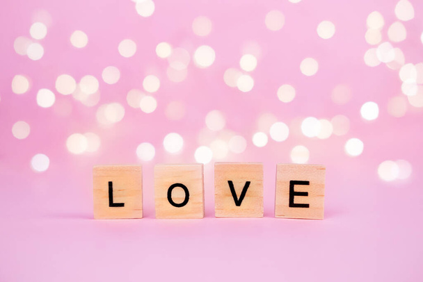 Words Love on a blurred pink background with a beautiful bokeh from a gold garland and lights. Place for the text, copyspace. Concept of holidays valentines day, mothers day, fathers day and romance - Fotó, kép