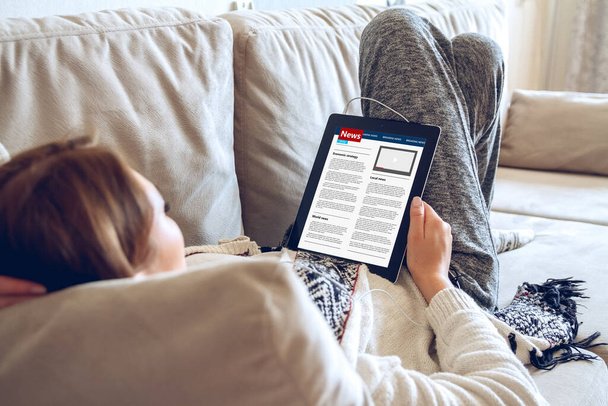 Nainen kotona kodikas vaatteita makaa sohvalla käyttäen tabletin kuulokkeet. Online koulutus käsite. e-oppiminen. taustakuva - Valokuva, kuva