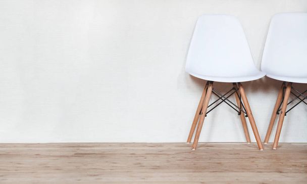 White plastic chair with wooden legs on a wooden floor against a white wall - 写真・画像