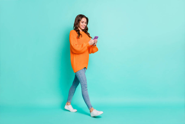 Full size profile side photo of young beautiful positive smiling girl go walk using smartphone isolated on teal color background - 写真・画像