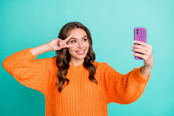 Photo of young girl happy smile make selfie cellphone show peace cool v-sign isolated over teal color background - Foto, immagini