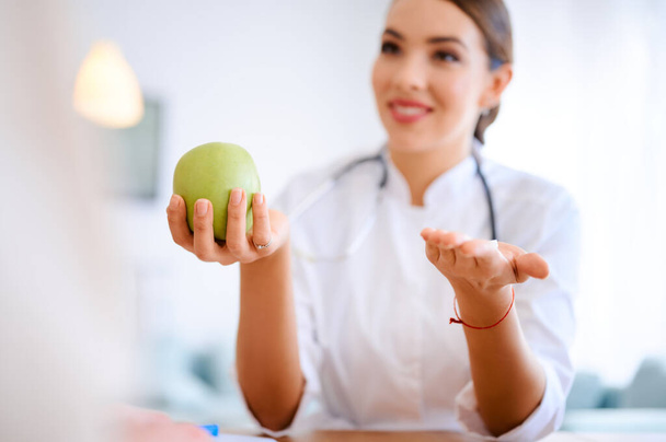 Kobieta lekarz trzyma jabłko i pigułki podczas dyskusji z pacjentem w biurze w szpitalu. Wysokiej jakości zdjęcie - Zdjęcie, obraz
