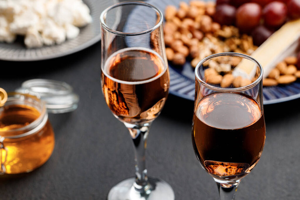 Glass of wine and plate with nuts on black table - Φωτογραφία, εικόνα