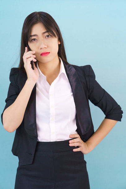 Young Asian women in suit standing posing using her phone against blue background - Foto, Imagen