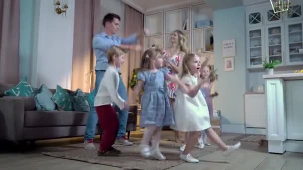 Ein glücklicher Familienvater und mehrere Kinder tanzten zu Hause in festlichen Outfits. Sie feiern ihren Geburtstag haben Spaß und springen - Filmmaterial, Video