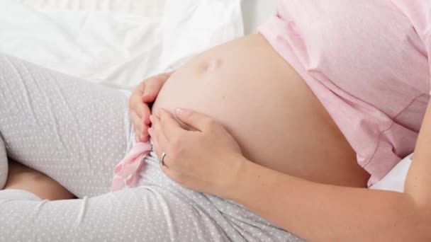 Primo piano di bella donna incinta in pigiama sdraiata a letto al mattino e accarezzando la sua grande pancia - Filmati, video