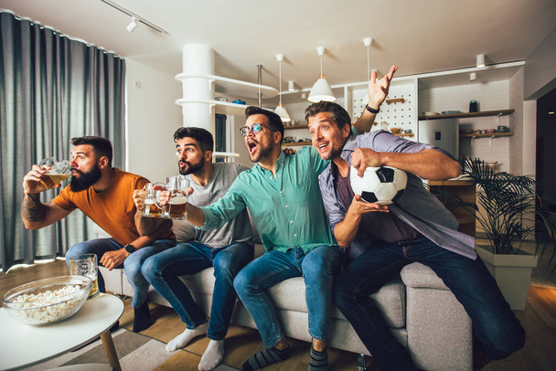 Amigos felices y aficionados al fútbol viendo fútbol en la televisión y celebrando la victoria en casa - Foto, Imagen