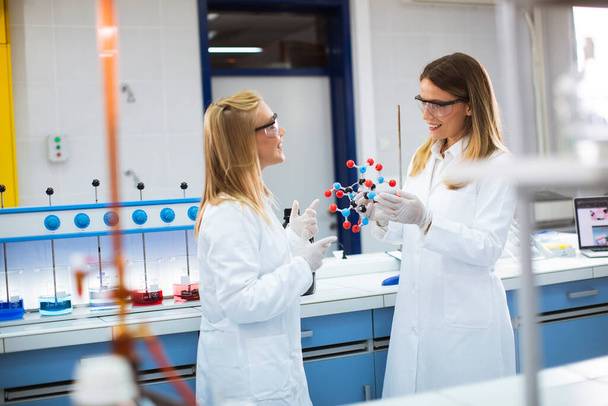 Vrouwelijke chemici met veiligheidsbril houden moleculair model in het lab - Foto, afbeelding