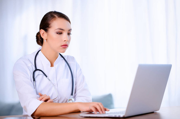 Medico donna con stetoscopio indossando cappotto da laboratorio lavora in ospedale e utilizzando il computer portatile - Foto, immagini