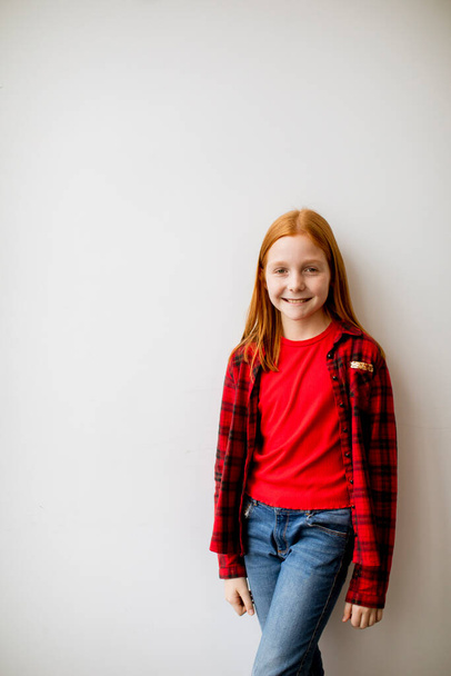 Χαριτωμένο κορίτσι με κόκκινα μαλλιά που στέκεται δίπλα στον λευκό τοίχο. - Φωτογραφία, εικόνα