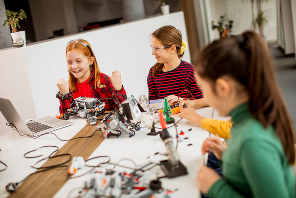 Groupe d'enfants heureux programmant des jouets électriques et des robots dans une salle de classe de robotique - Photo, image