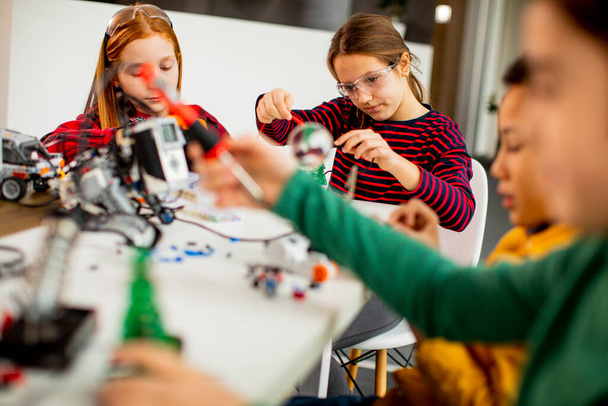Ομάδα χαρούμενων παιδιών που προγραμματίζουν ηλεκτρικά παιχνίδια και ρομπότ στην τάξη ρομποτικής - Φωτογραφία, εικόνα