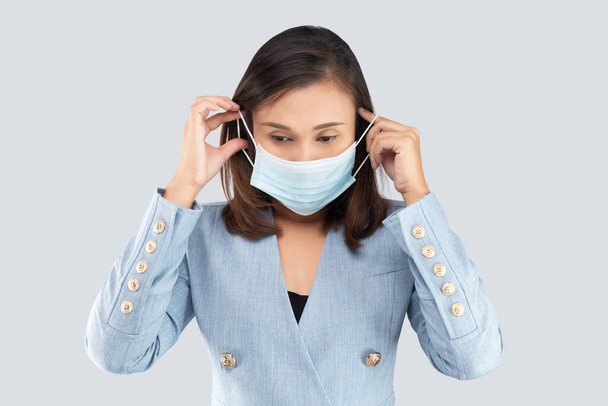 Ασιάτισσα επιχειρηματίας που φοράει ιατρική μάσκα και είναι απομονωμένη σε γκρι φόντο. - Φωτογραφία, εικόνα