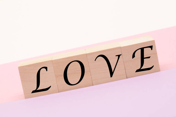 de woorden liefde op houten blokjes op een pastelachtergrond. Het concept van liefde en Valentijnsdag - Foto, afbeelding