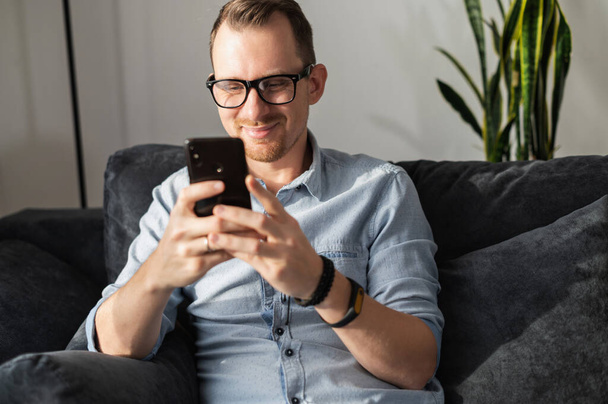 A guy with a smartphone sits on the couch - Fotoğraf, Görsel