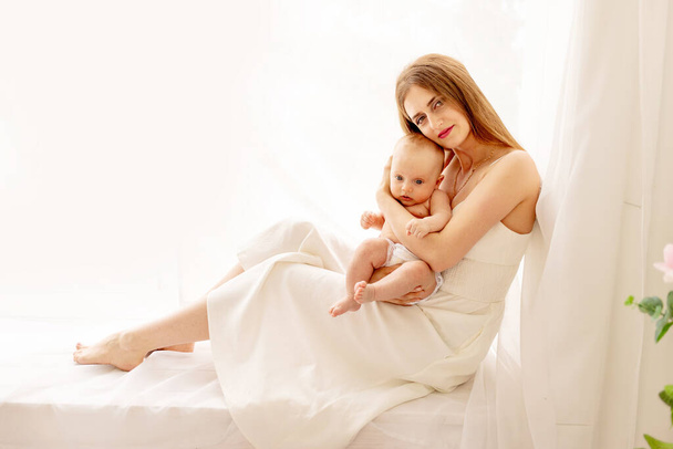 mamá con el bebé en brazos en casa en la ventana, el concepto de familia y maternidad - Foto, imagen