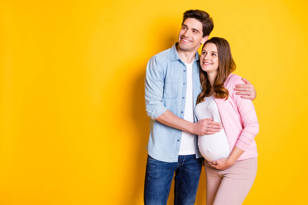 Photo of optimistic young couple stand hug look empty space pregnant woman wear casual outfits isolated on yellow color background - Fotó, kép