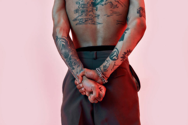Tattoos showing. Two hands holding each other behind a back of a dark-skinned tattooed man standing - 写真・画像