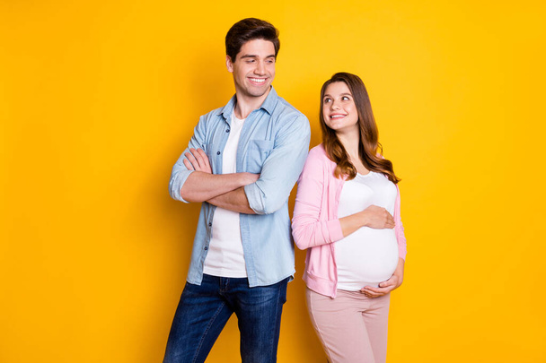 Photo of attractive pair expecting child father arms folded mommy hugging belly looking each other isolated yellow color background - Φωτογραφία, εικόνα