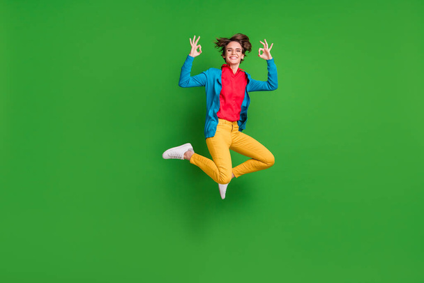 Full length body size photo of happy girl jumping high showing okay sign smiling isolated on vivid green color background - Фото, зображення