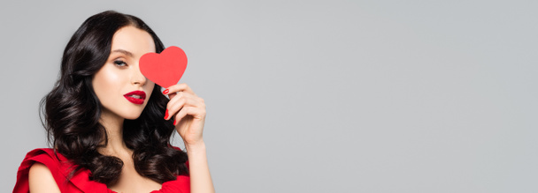 Genç esmer kadın göz kapağı kırmızı kağıt kalp gri, afişte izole - Fotoğraf, Görsel