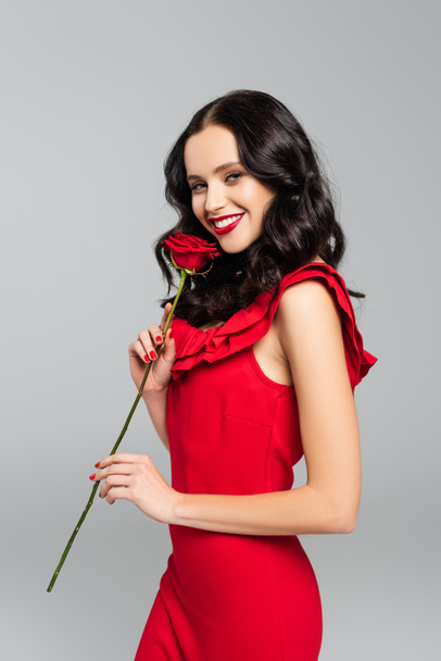 joyful young woman holding red rose isolated on grey  - Фото, изображение